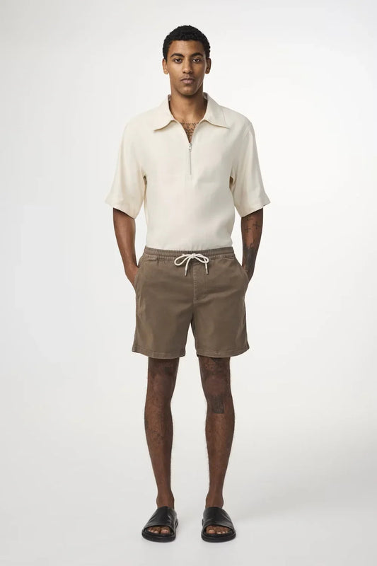 Man i beige pikétröja och bruna shorts med dragsko, herrmode sommarstil
