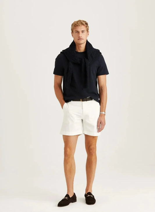 Man i stilren herroutfit med svarta loafers, mörk t-shirt och vita chinoshorts.