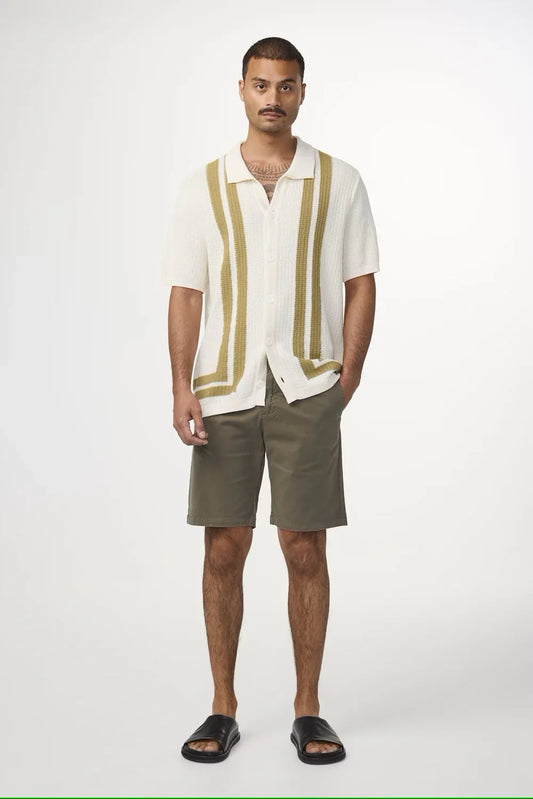 Man i vit kortärmad skjorta med gröna ränder, olivgröna shorts och svarta sandaler