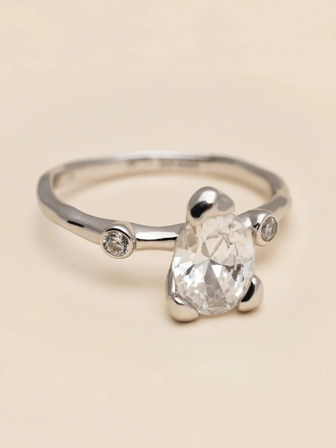 Elegant silverring med stor dropformad klar sten och två små runda stenar mot ljus bakgrund.