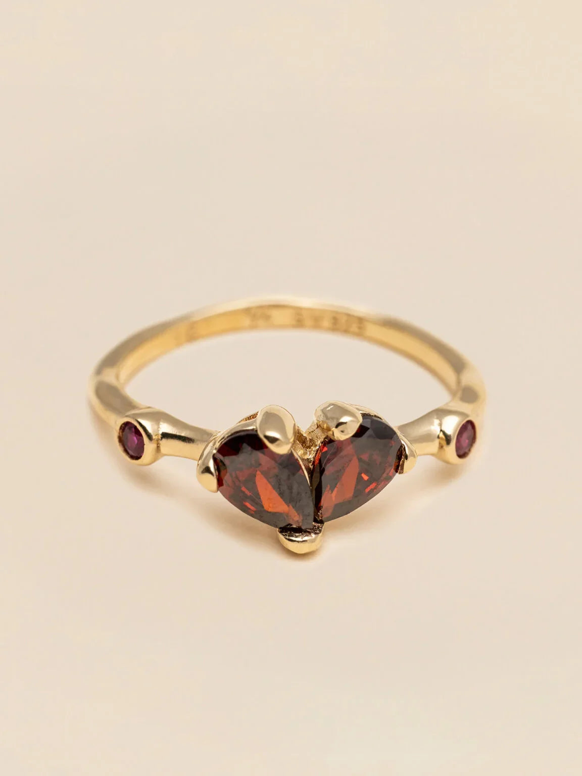 Guldring med röda hjärtformade stenar och små lila ädelstenar, elegant design.