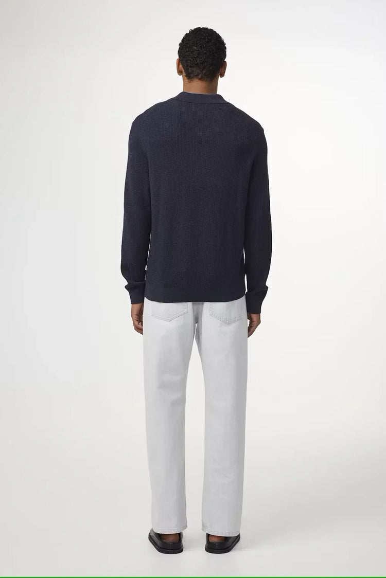 Man i mörkblå stickad tröja och ljusa raka jeans, sedd bakifrån mot vit bakgrund
