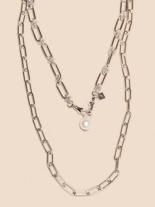 Silverfärgat halsband med stora länkar och hänge med vit pärla på beige bakgrund