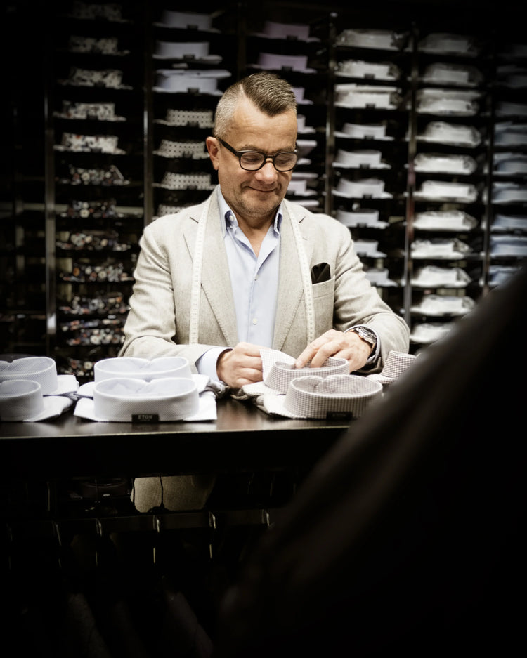 Välklädd man provar eleganta skjortkragar i herrklädesbutik med skjortor i bakgrunden