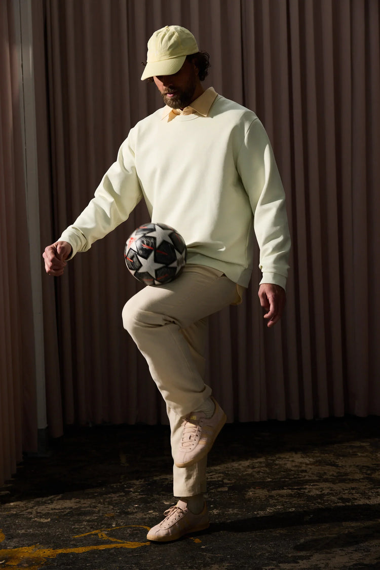 Ljusgul sweatshirt herr, beigefärgade byxor, beige keps, sneakers