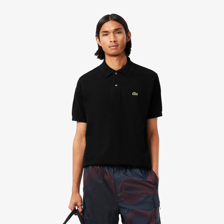 Man i svart pikétröja och sportiga mönstrade shorts, klassisk herrklädstil