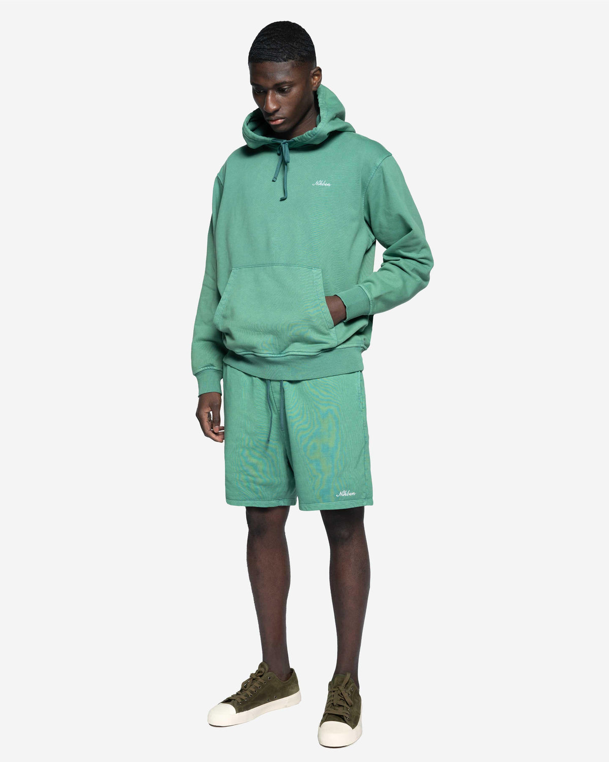 Man i grön hoodie och matchande shorts, avslappnad herrklädstil, vit bakgrund