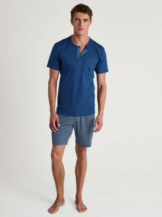 Man i blå kortärmad pyjamas med mönstrade shorts mot vit bakgrund