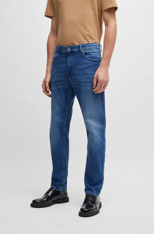 Herr i blå jeans, brun t-shirt och svarta skor mot ljus bakgrund