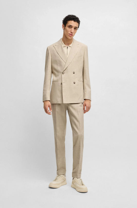 Man i beige dubbelknäppt kostym, matchande byxor och sneakers mot ljus bakgrund.