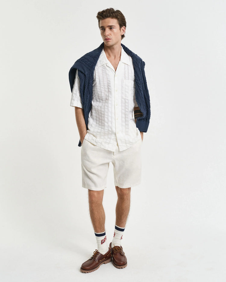 Man i vit kortärmad skjorta och shorts, blå tröja över axlarna, bruna seglarskor