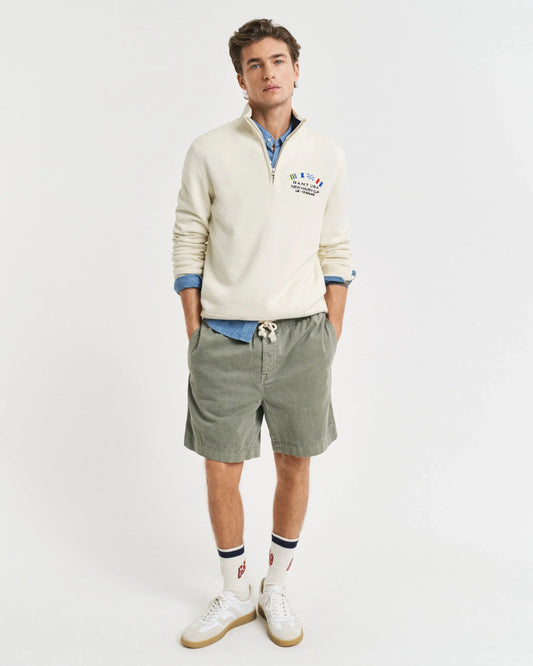 Man i klassisk herrstil med vit tröja, skjorta, gröna shorts och vita sneakers på vit bakgrund