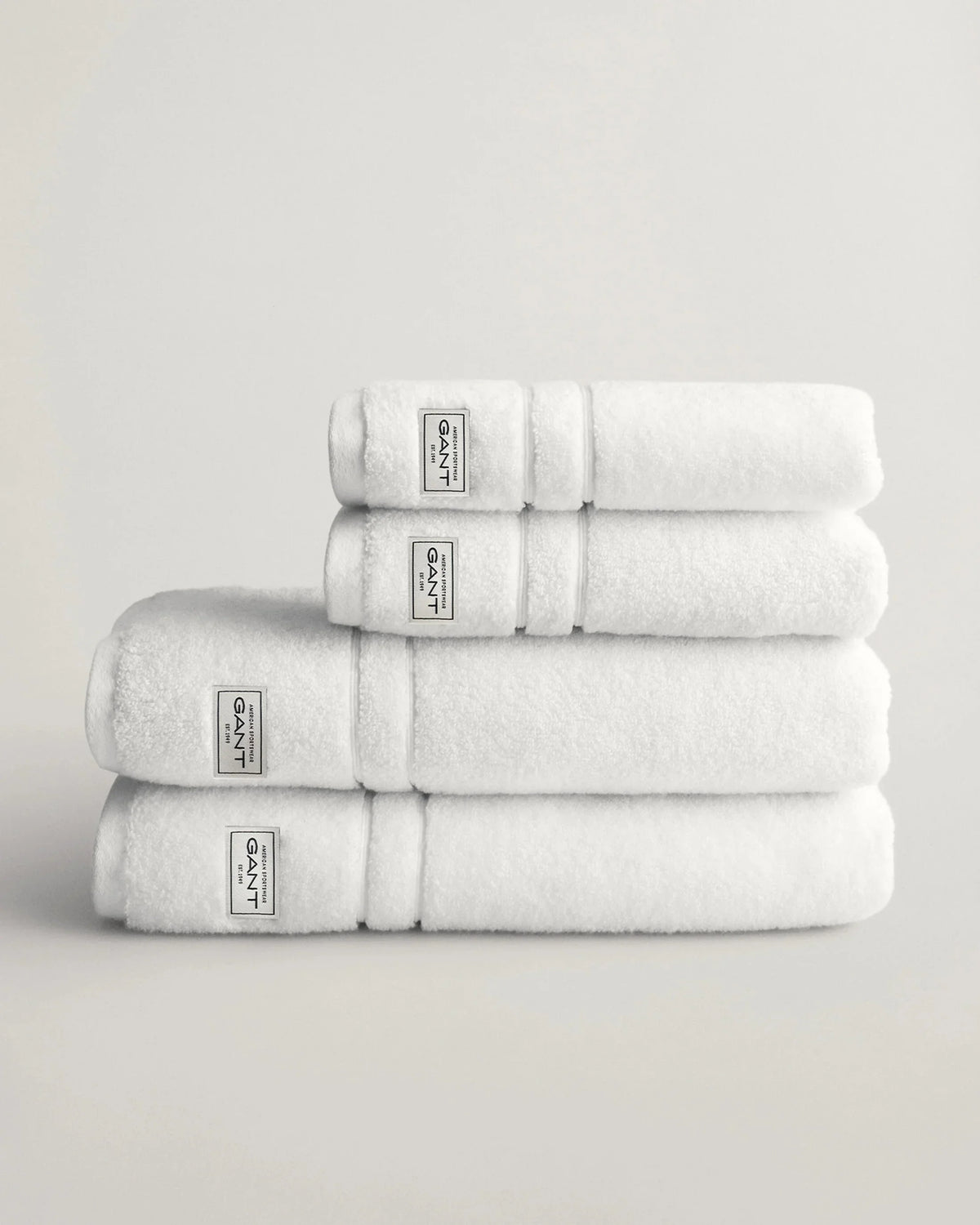 Vita handdukar i frotté staplade på varandra mot ljus bakgrund, herrtextil och accessoar.