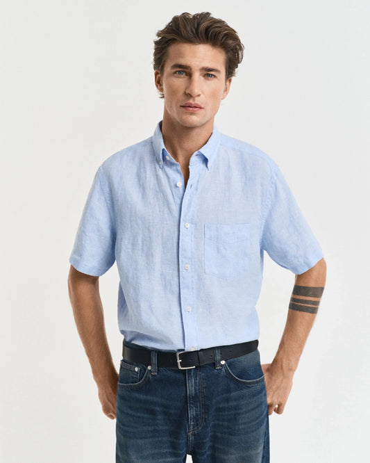 Man i ljusblå kortärmad linneskjorta och blå jeans mot vit bakgrund