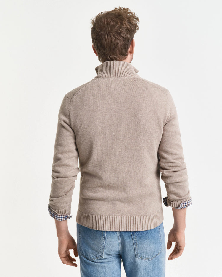 Man bakifrån i beige stickad tröja och ljusblå jeans mot vit bakgrund.