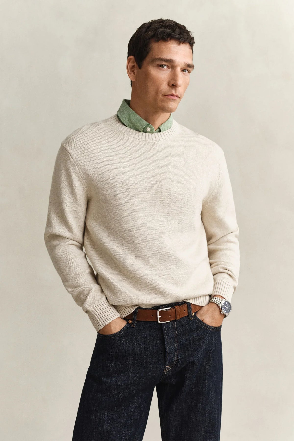 Beige stickad herrtröja, grön skjorta och mörkblå jeans