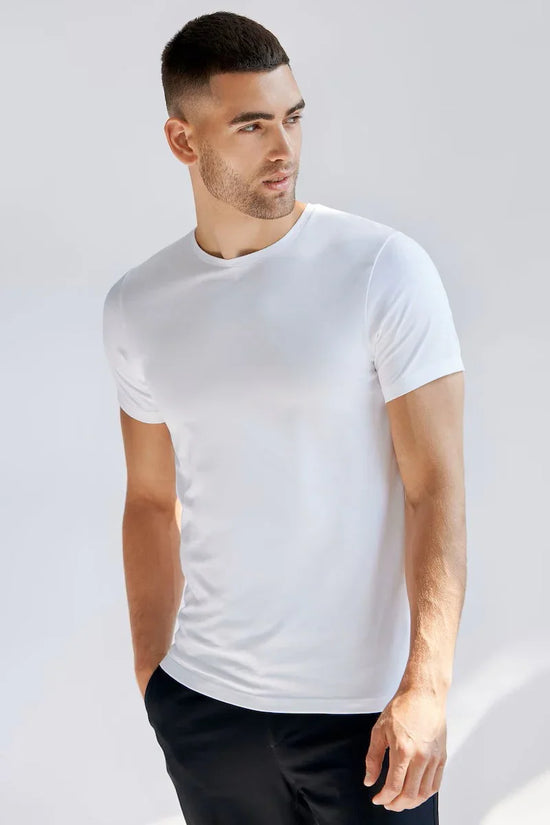 Man i vit t-shirt med rund hals, klassiskt herrmode mot ljus bakgrund