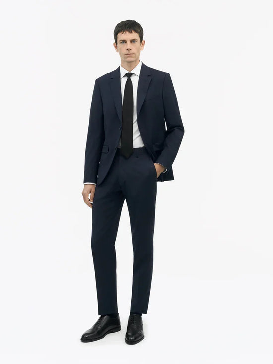 Man i mörkblå kostym, vit skjorta och svart slips, klassisk herrmode på vit bakgrund.