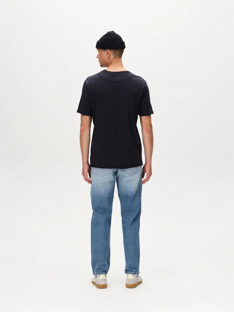 Man i svart t-shirt, jeans och mössa fotad bakifrån mot vit bakgrund