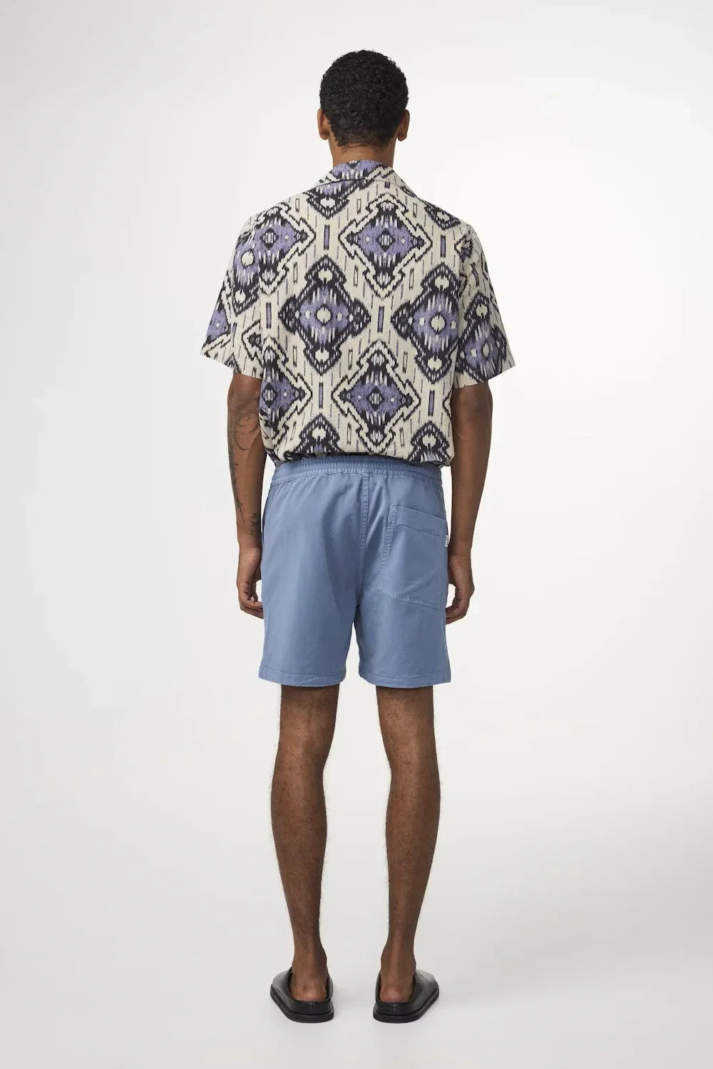 Man i mönstrad skjorta och ljusblå shorts, sommaroutfit för herr i studiomiljö
