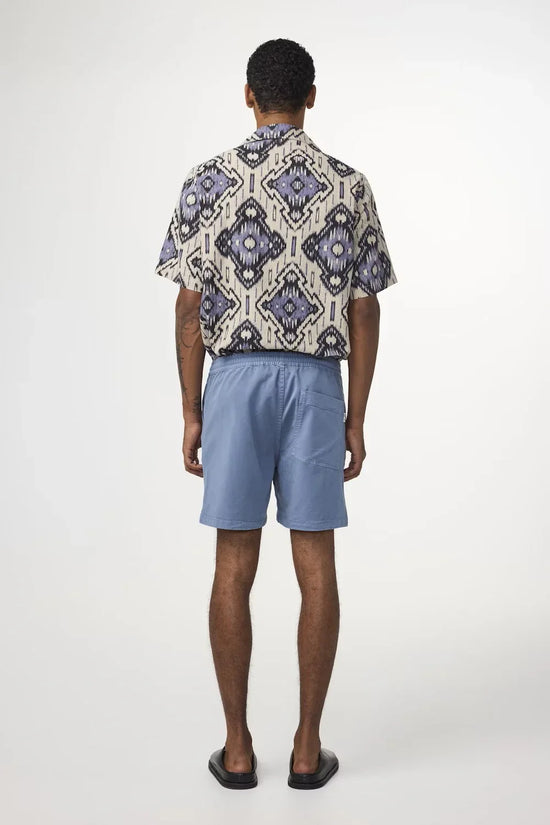 Man i mönstrad skjorta och ljusblå shorts, sommaroutfit för herr i studiomiljö