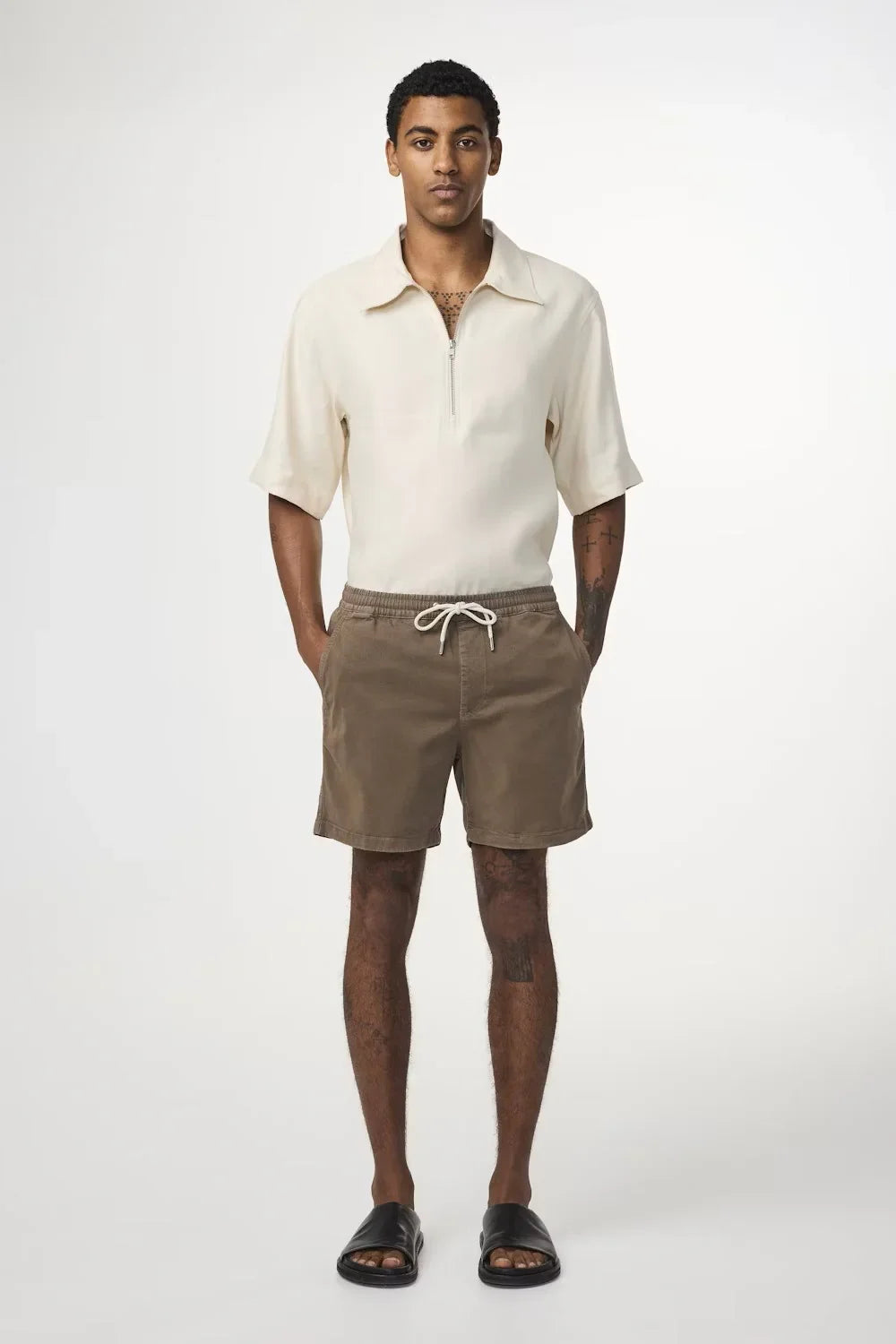 Man i beige pikétröja och bruna shorts med dragsko, herrmode sommarstil