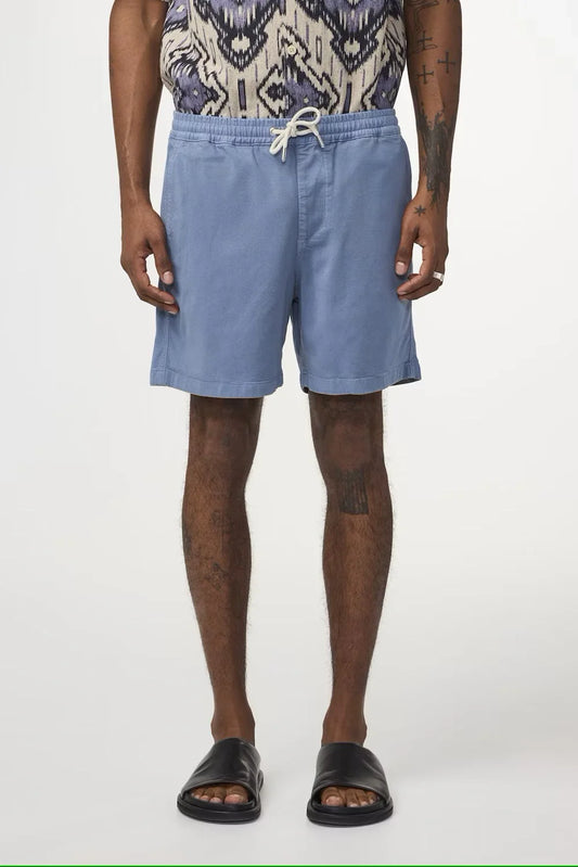 Herr i ljusblå shorts med dragsko, mönstrad skjorta och svarta sandaler på vit bakgrund