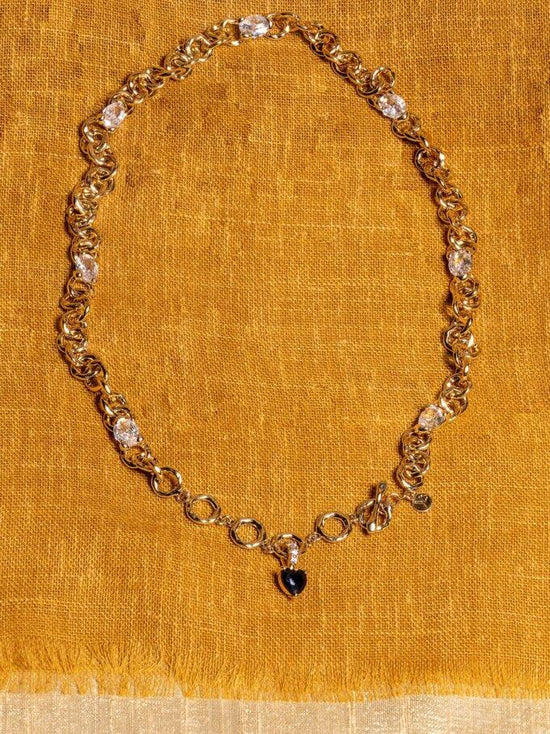 Guldfärgat halsband med klara stenar och svart hängsmycke på senapsgul textil