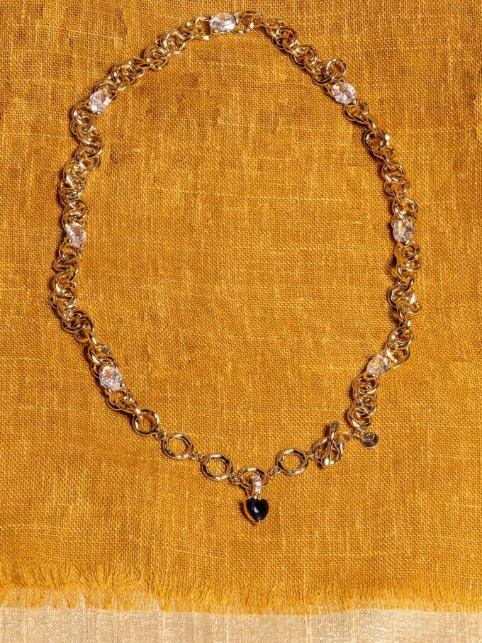 Guldfärgat halsband med klara stenar och svart hängsmycke på senapsgul textil