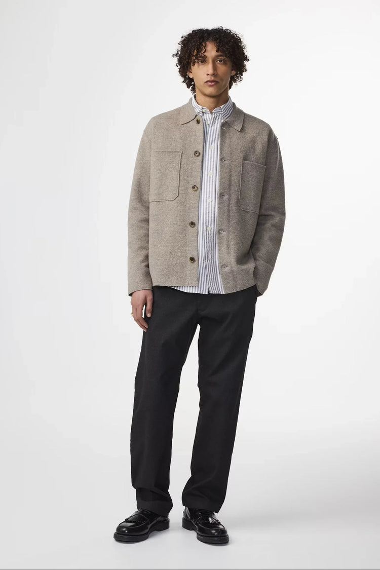 Beige herr jacka med knappar och stora fickor, bärs över randig skjorta och svarta byxor.
