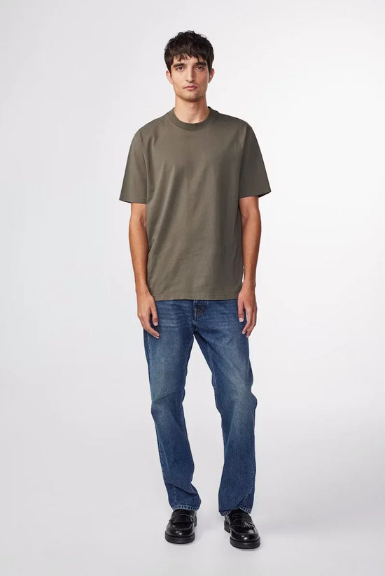 Man i khakigrön t-shirt och blå jeans, klassisk herrklädstil mot vit bakgrund