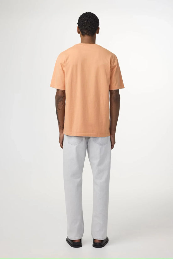 Man med kortärmad persikofärgad t-shirt och ljusa jeans, syns bakifrån mot vit bakgrund