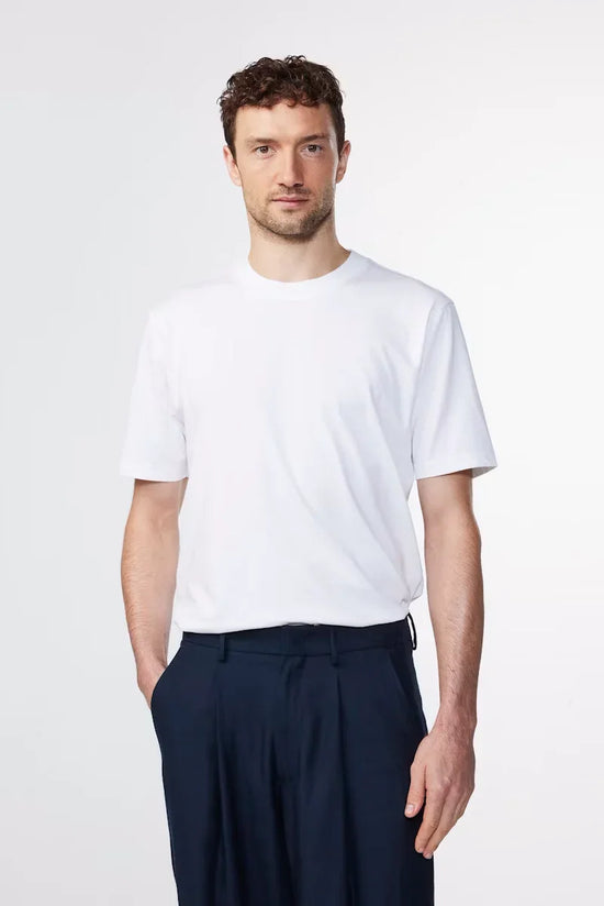 Man i vit t-shirt och mörkblå byxor mot ljus bakgrund, klassiskt herrmode