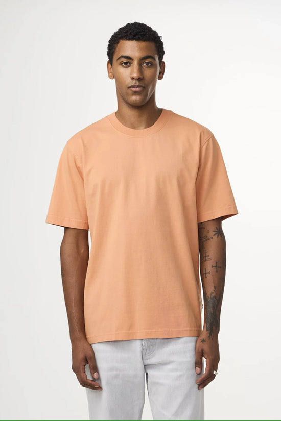 Man i persikofärgad t-shirt och ljusa jeans mot vit bakgrund, herrmode klassiskt stilren
