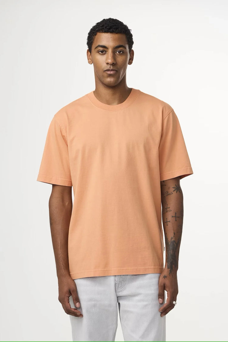 Man i persikofärgad t-shirt och ljusa jeans mot vit bakgrund, herrmode klassiskt stilren