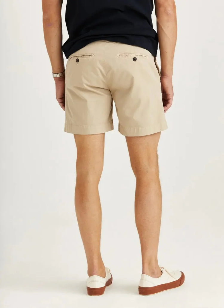 Herrmodell bär beige chinoshorts med bakfickor, vit sneaker och mörk tröja, sommarstil.