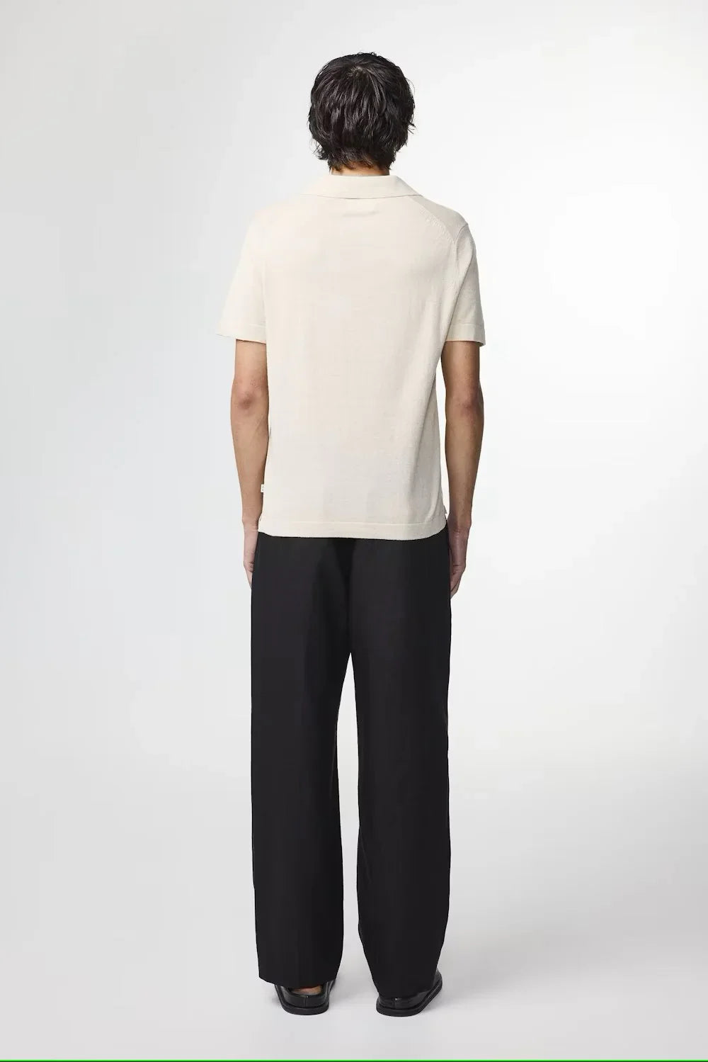 Man i beige pikétröja och svarta byxor, sedd bakifrån, klassisk herrstil