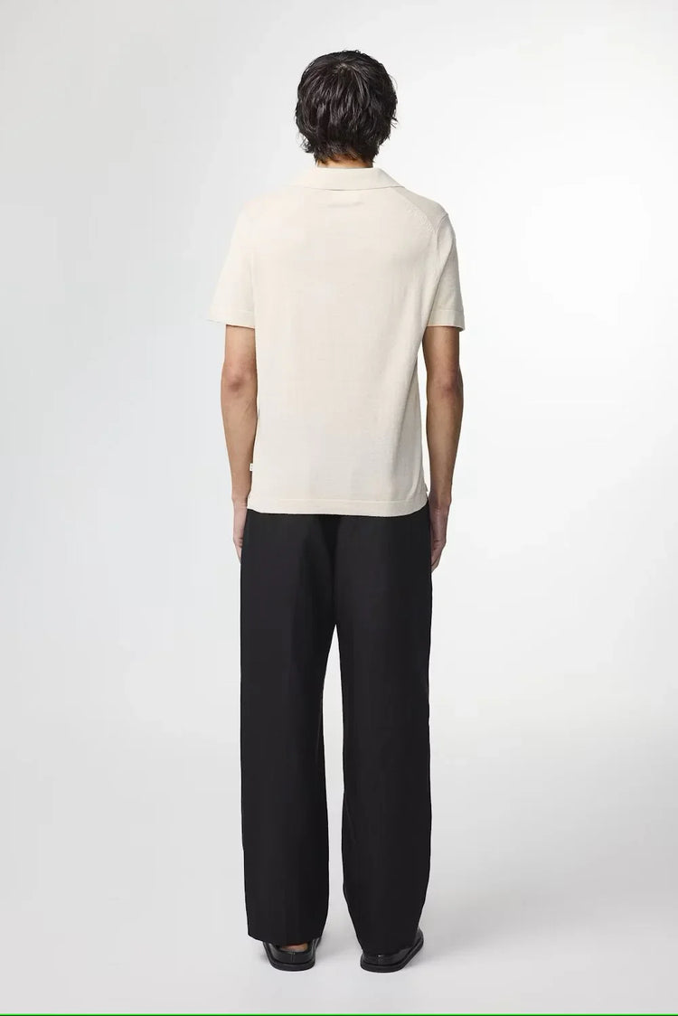 Man i beige pikétröja och svarta byxor, sedd bakifrån, klassisk herrstil