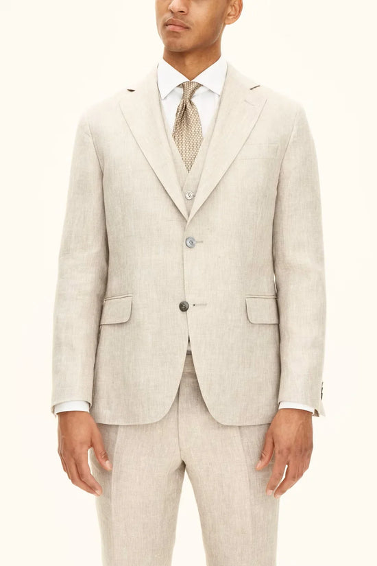 Man i ljusbeige linneblazer, väst och byxor, vit skjorta och mönstrad slips