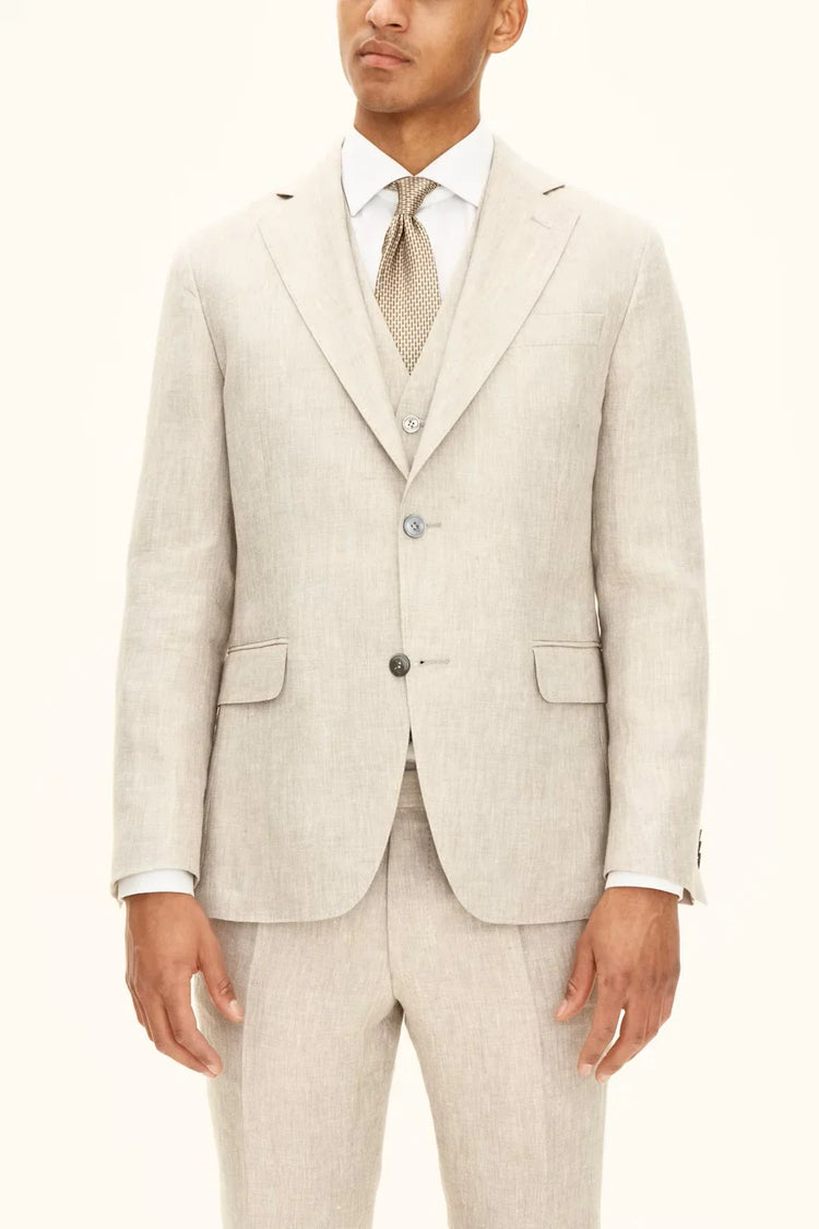 Man i ljusbeige linneblazer, väst och byxor, vit skjorta och mönstrad slips