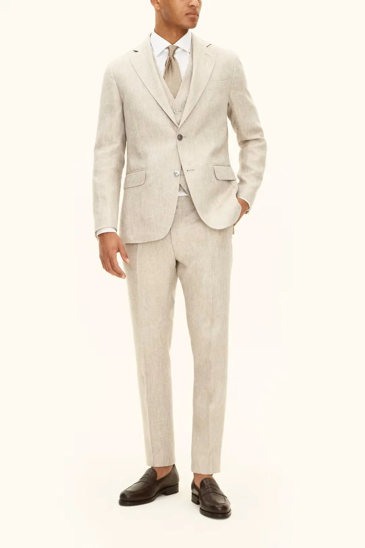 Man i ljusbeige kostym med väst och slips, klassisk herrstil mot vit bakgrund.