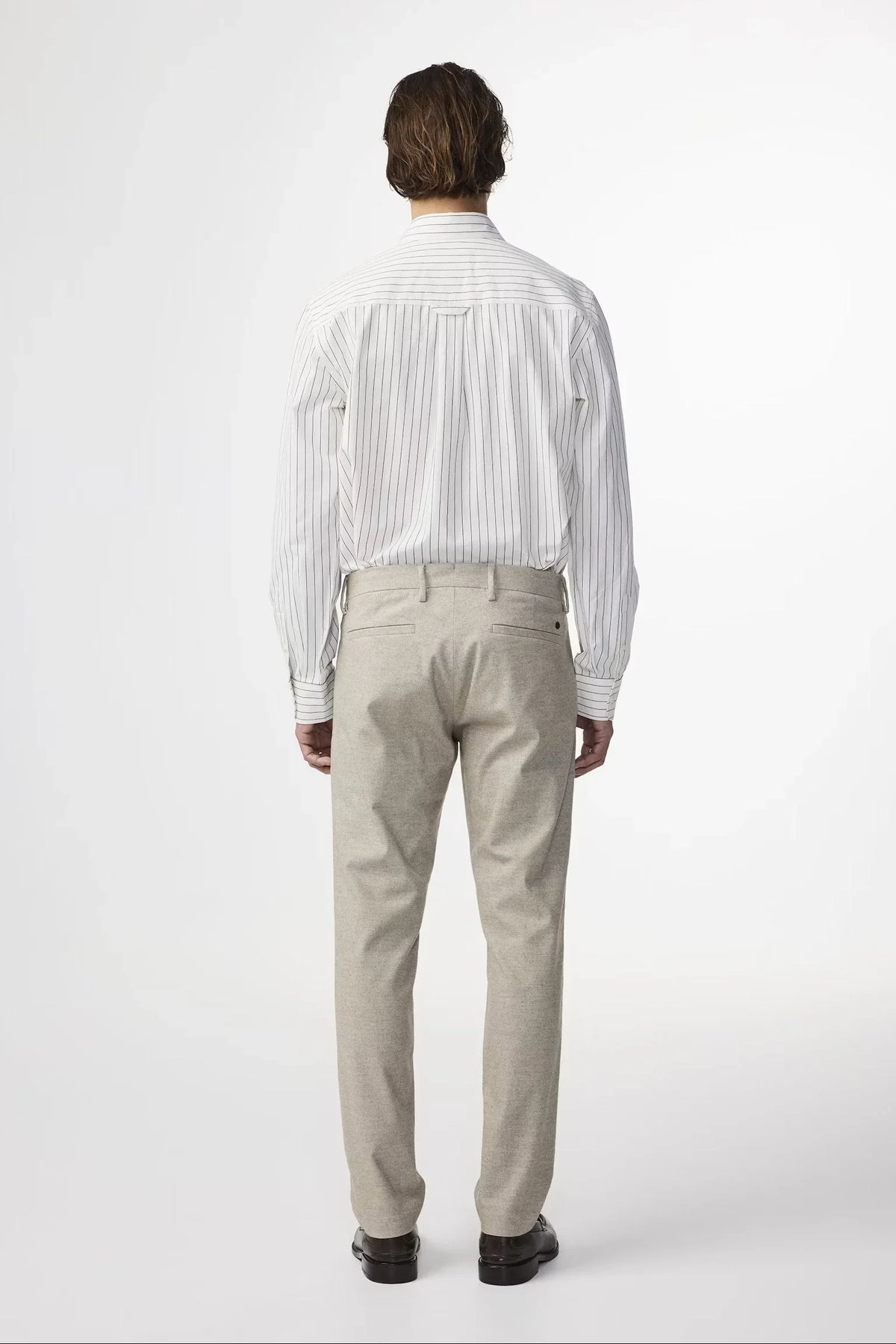 Bakre vy av herrkostymbyxor i beige, klassiskt snitt, på modell i skjorta.