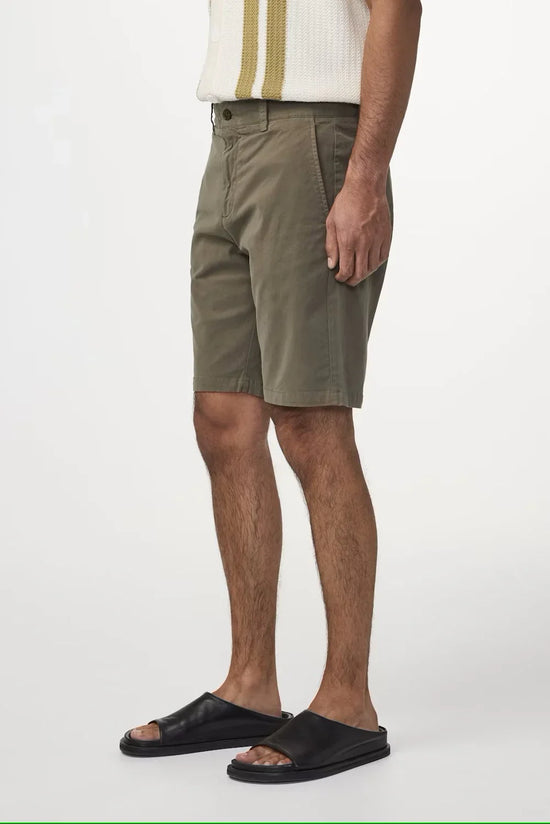 Herrben klädd i gröna shorts och svarta sandaler mot vit bakgrund