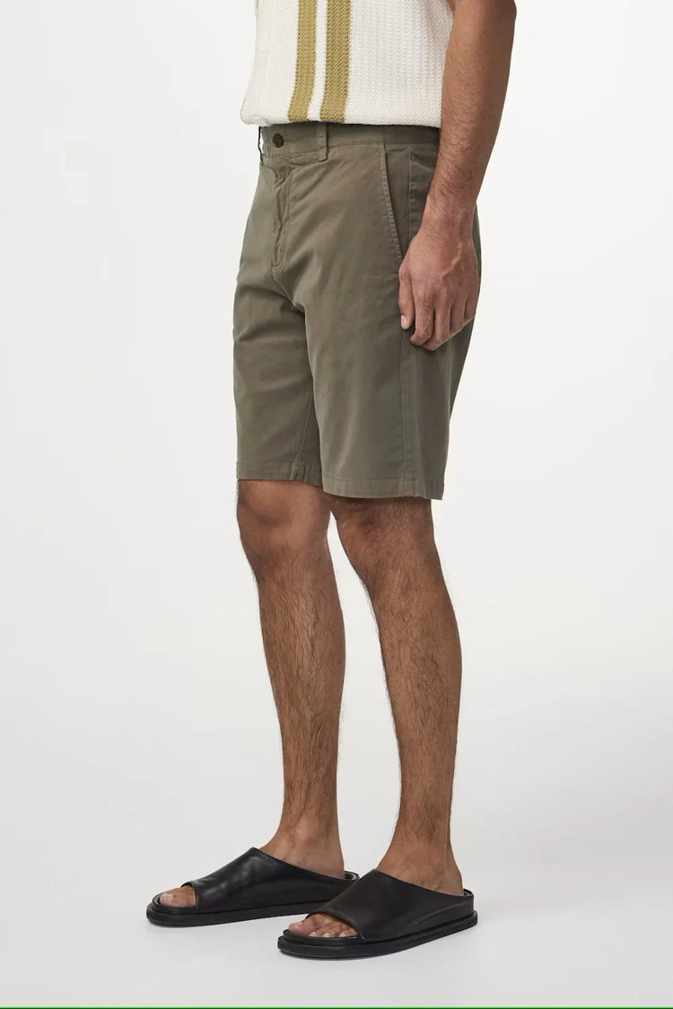 Herrben klädd i gröna shorts och svarta sandaler mot vit bakgrund
