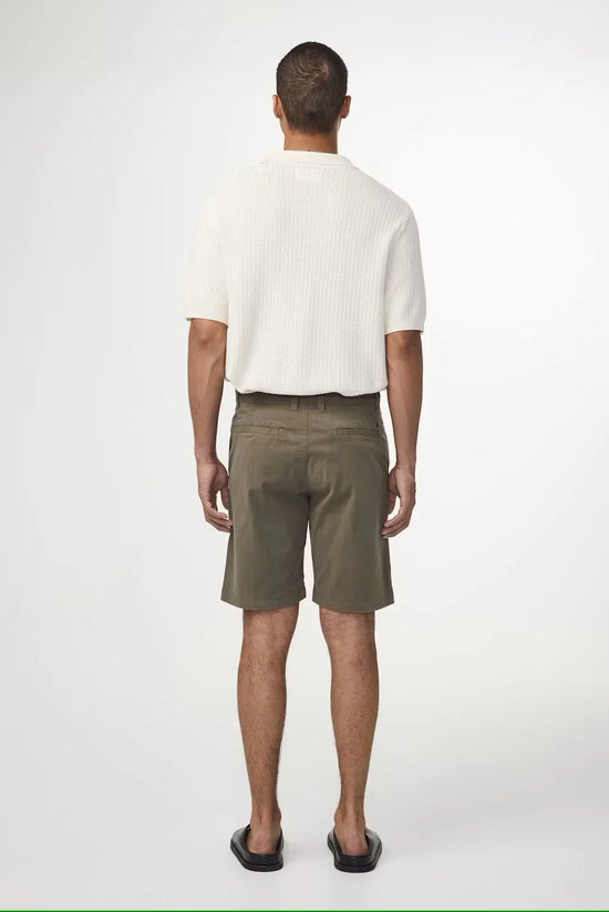 Man i vita pikétröja och olivgröna herrshorts sedd bakifrån på vit bakgrund