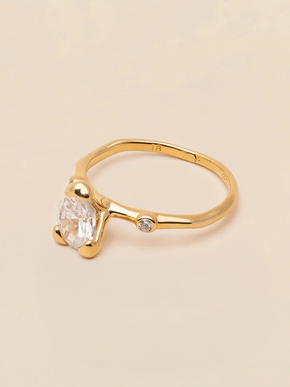 Elegant guldring med oval klar sten och liten rund diamant på ljus bakgrund