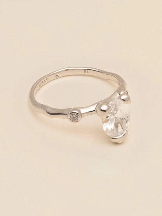 Elegant silverring med stor klar sten och liten diamantdetalj på ljus bakgrund