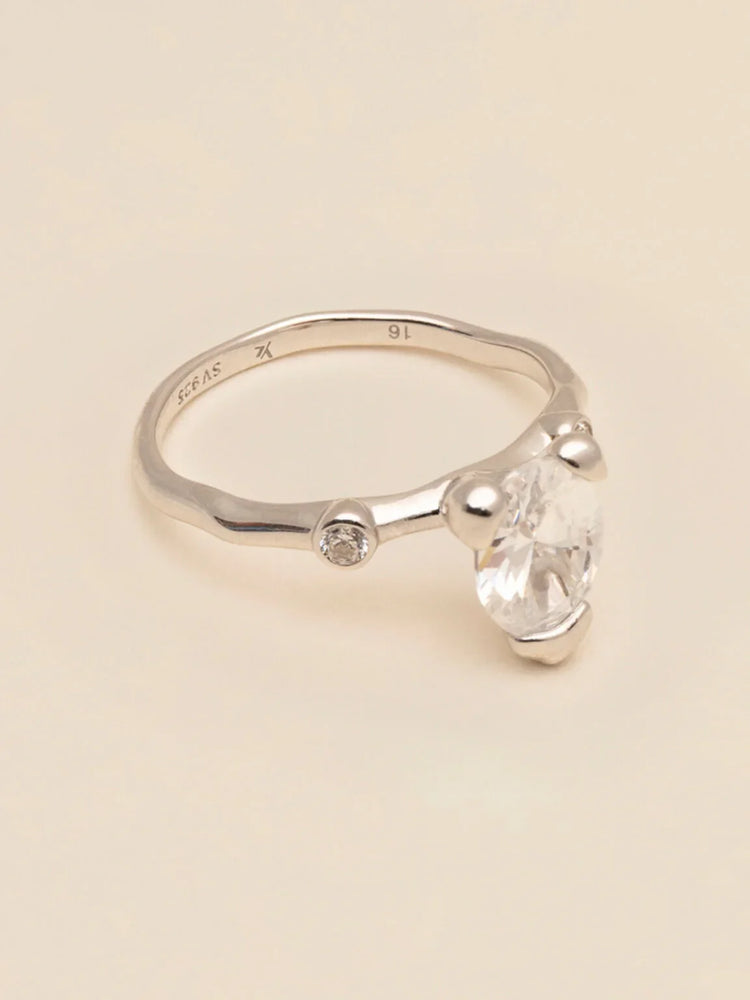 Elegant silverring med stor klar sten och liten diamantdetalj på ljus bakgrund