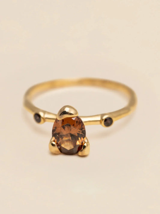 Elegant guld ring med brun oval sten, herrsmycke mot beige bakgrund