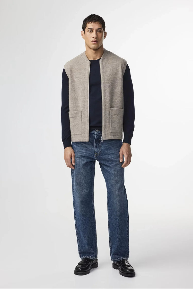 Beige stickad herr väst med fickor, klassisk stil, modell bär blå jeans och mörk tröja